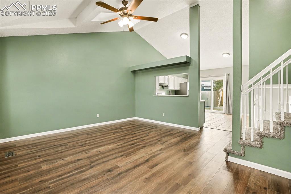 Unfurnished living room featuring ceiling fan, dark wood-style floors, and a high ceiling