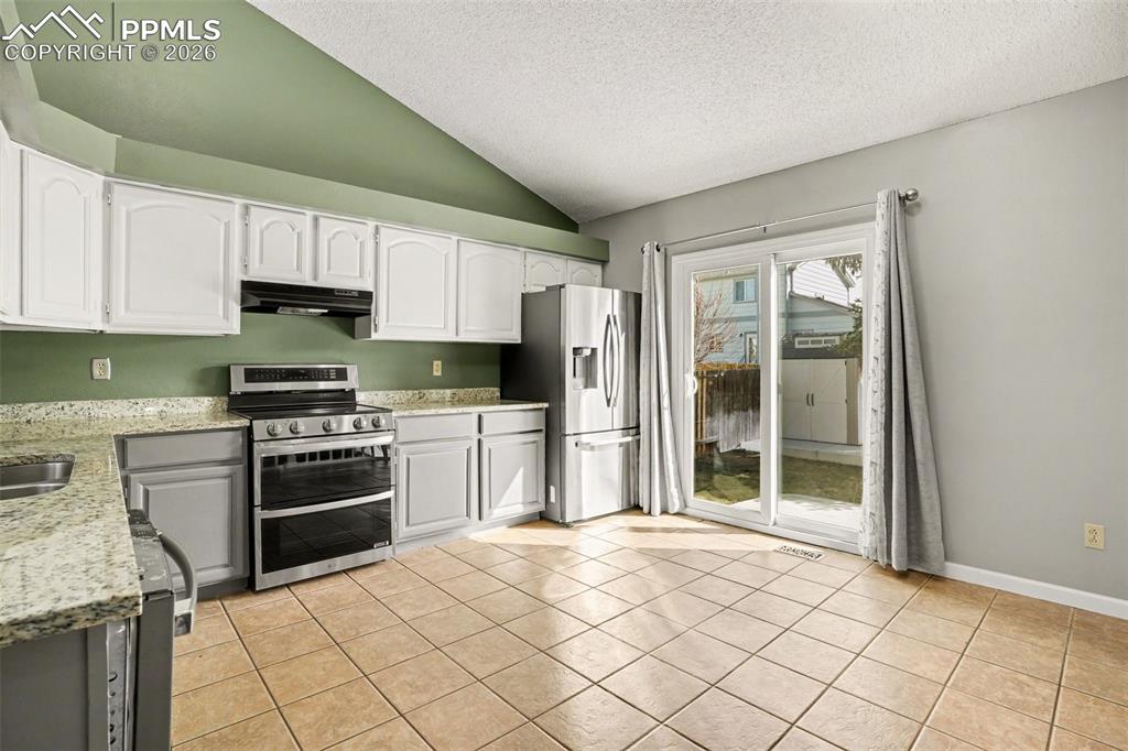 Kitchen with stainless steel appliances, light stone counters, white cabinetry, and light tile patterned floors