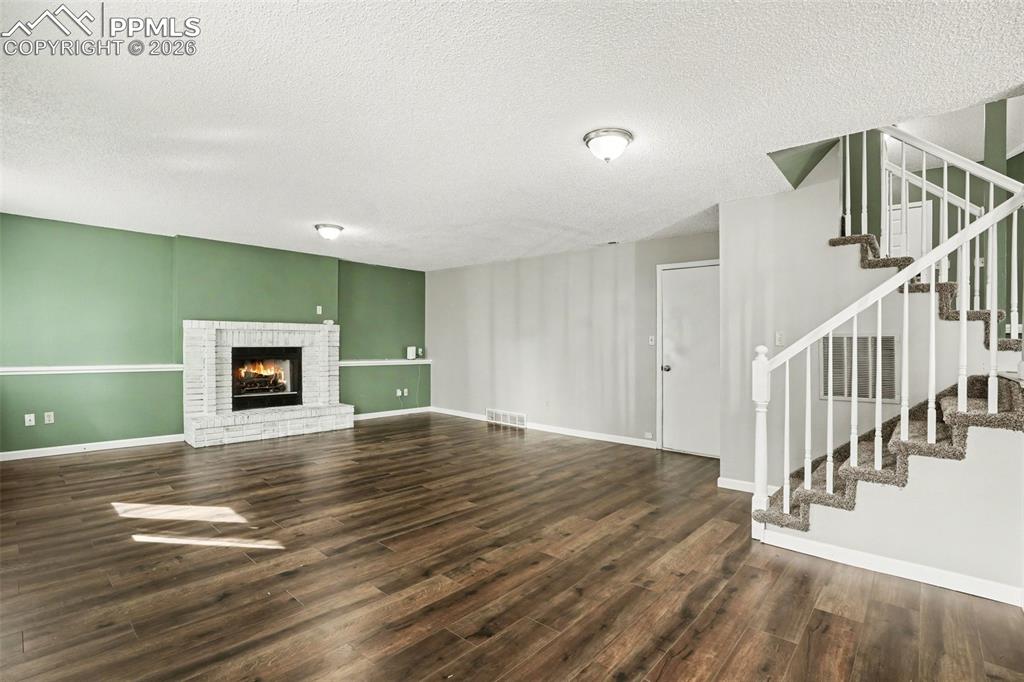 Unfurnished living room featuring dark wood-style floors, a brick fireplace, and a textured ceiling