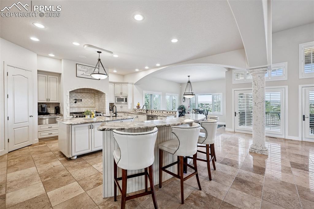 Kitchen with a large island, stainless steel microwave, decorative columns, recessed lighting, and decorative backsplash