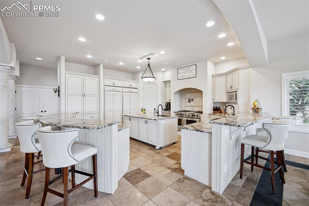 Kitchen with a kitchen island with sink, stainless steel appliances, a kitchen bar, a peninsula, and recessed lighting