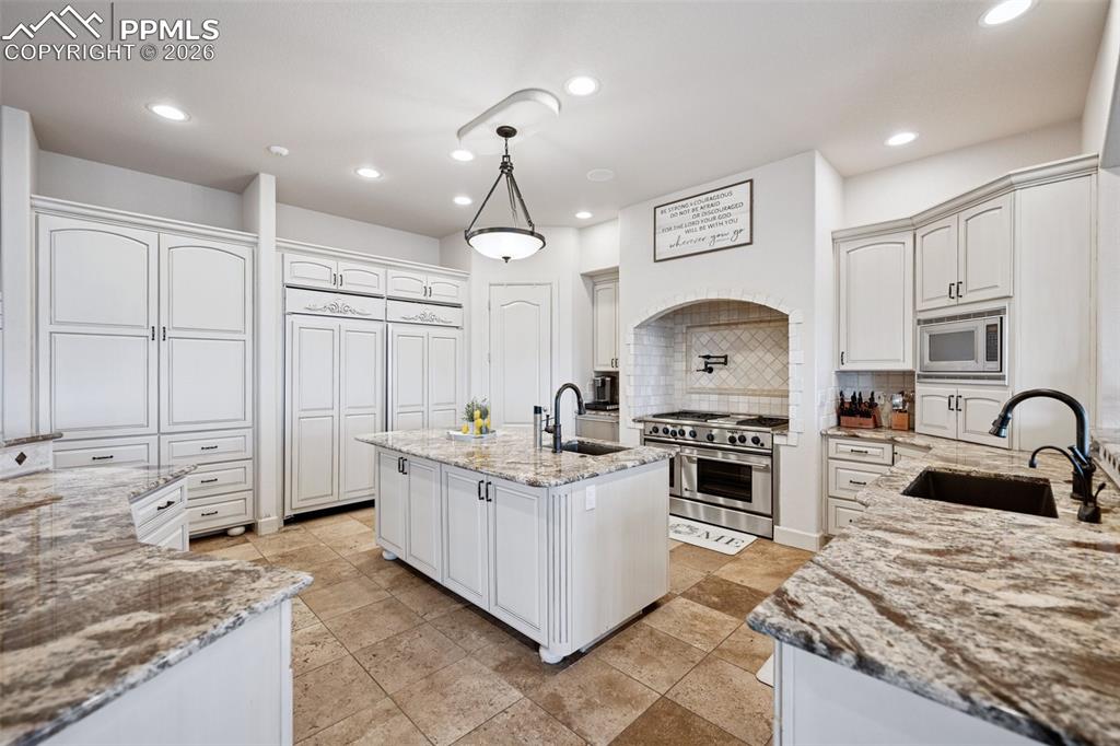 Kitchen with stainless steel appliances, a sink, backsplash, and light stone counters