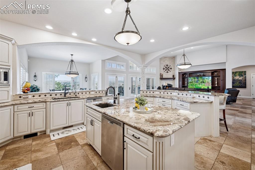 Kitchen featuring arched walkways, a kitchen island with sink, appliances with stainless steel finishes, and a sink
