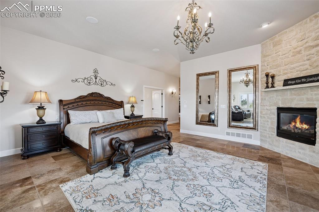 Bedroom with baseboards, a stone fireplace, visible vents, and a chandelier