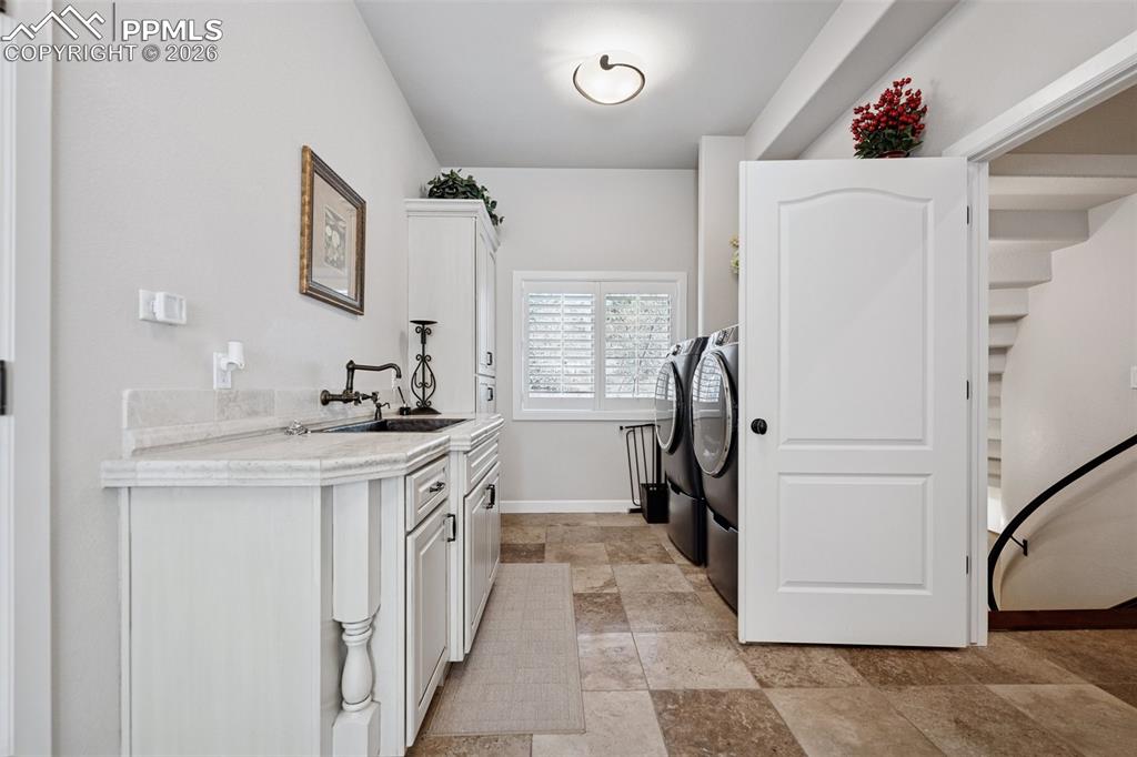 Clothes washing area featuring a sink, stone finish flooring, washing machine and dryer, baseboards, and laundry area