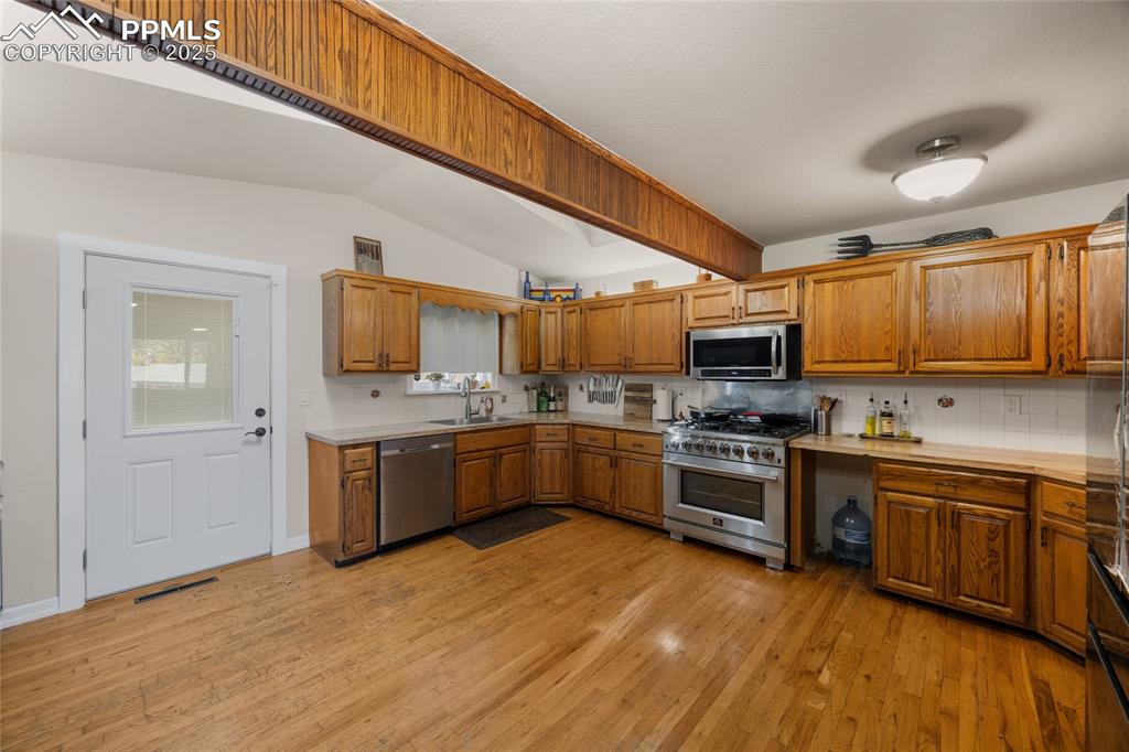Kitchen with decorative backsplash, light countertops, brown cabinets, light wood-style floors, and lofted ceiling