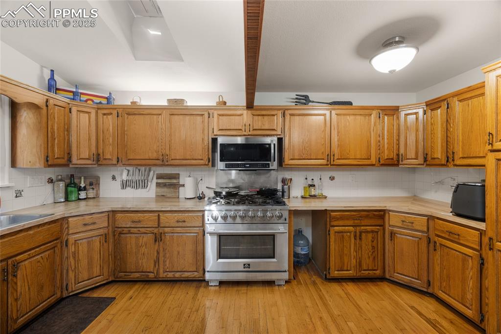 Kitchen featuring tasteful backsplash, light countertops, appliances with stainless steel finishes, light wood-style flooring, and beamed ceiling