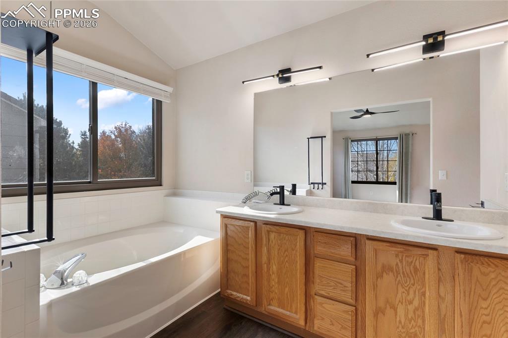 Full bath with a garden tub, vaulted ceiling, double vanity, and dark wood-style floors