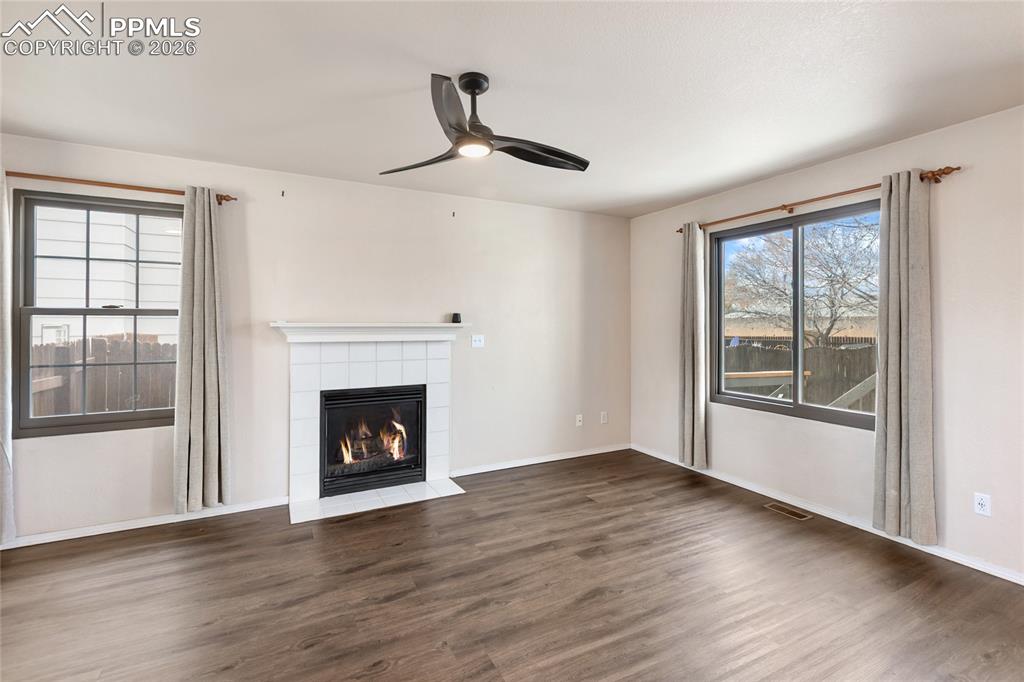 Unfurnished living room with dark wood finished floors, a tile fireplace, and ceiling fan