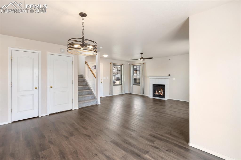 Unfurnished living room with a chandelier, dark wood-style flooring, stairway, a fireplace with flush hearth, and ceiling fan
