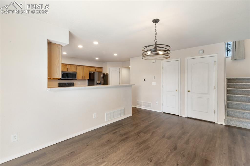 Kitchen with dark wood-style flooring, stainless steel appliances, recessed lighting, decorative light fixtures, and a peninsula