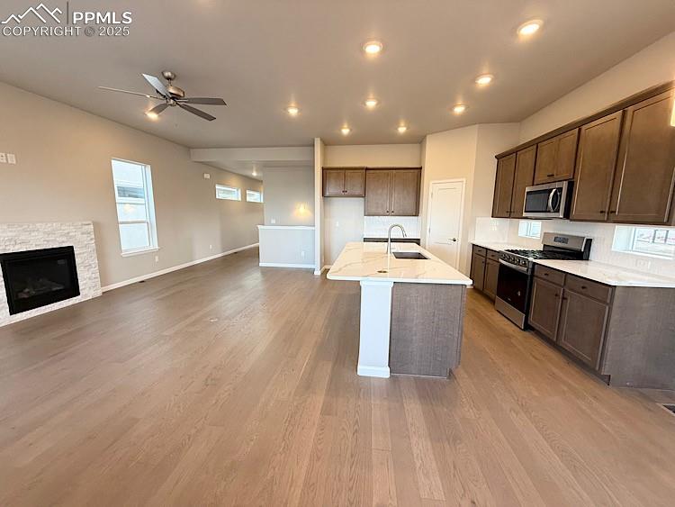 The Great room is open to the Kitchen and includes engineered wood flooring, floor outlet, ceiling fan, LED lighting, an abundance of natural light, and a gas fireplace with beautiful stacked stone surround!