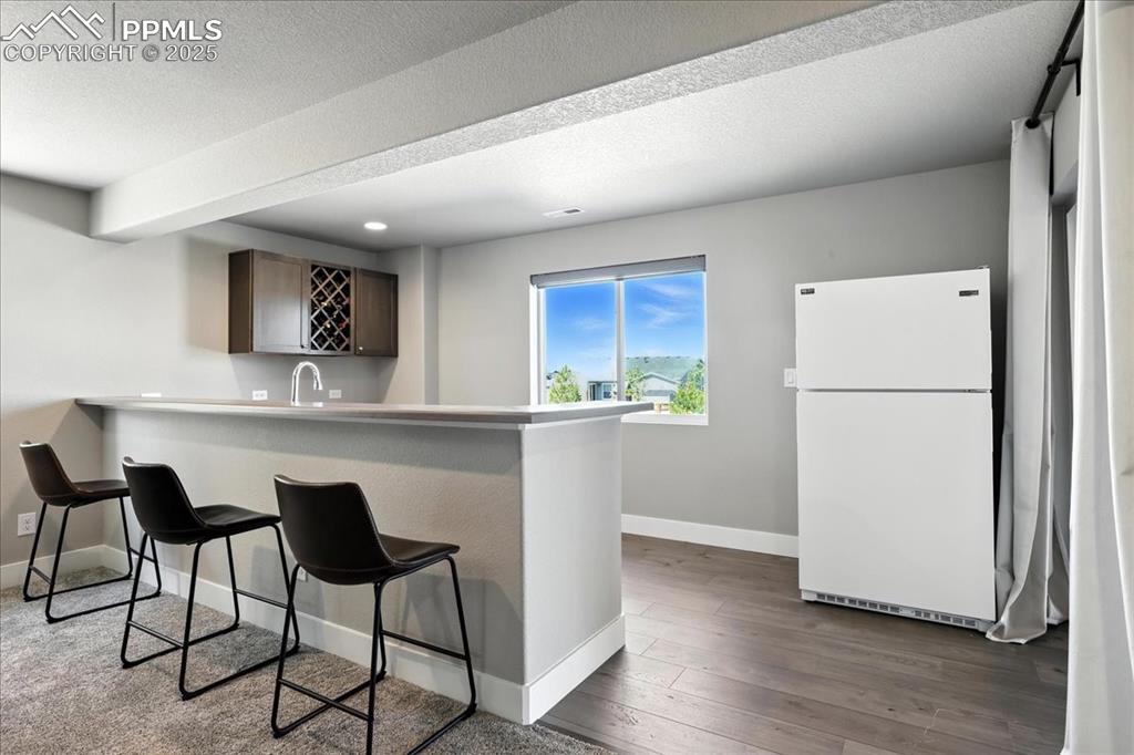 Kitchen with freestanding refrigerator, a kitchen bar, dark wood-style floors, a peninsula, and a textured ceiling