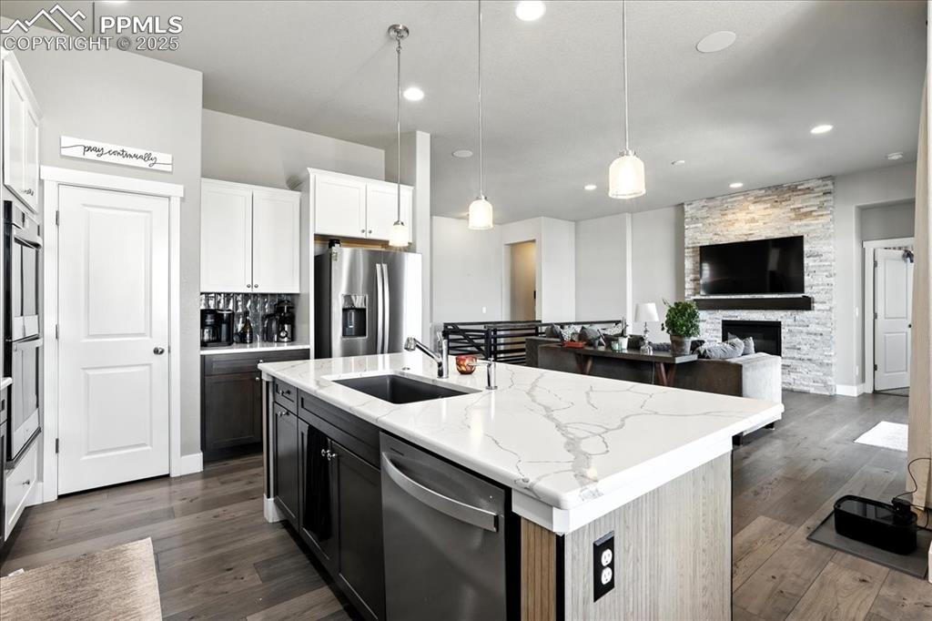 Kitchen featuring stainless steel appliances, dark wood-type flooring, a kitchen island with sink, a stone fireplace, and recessed lighting