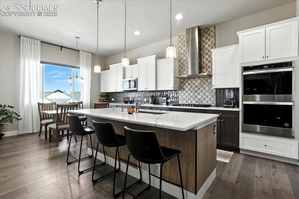 Kitchen featuring backsplash, stainless steel appliances, an island with sink, dark wood-type flooring, and recessed lighting