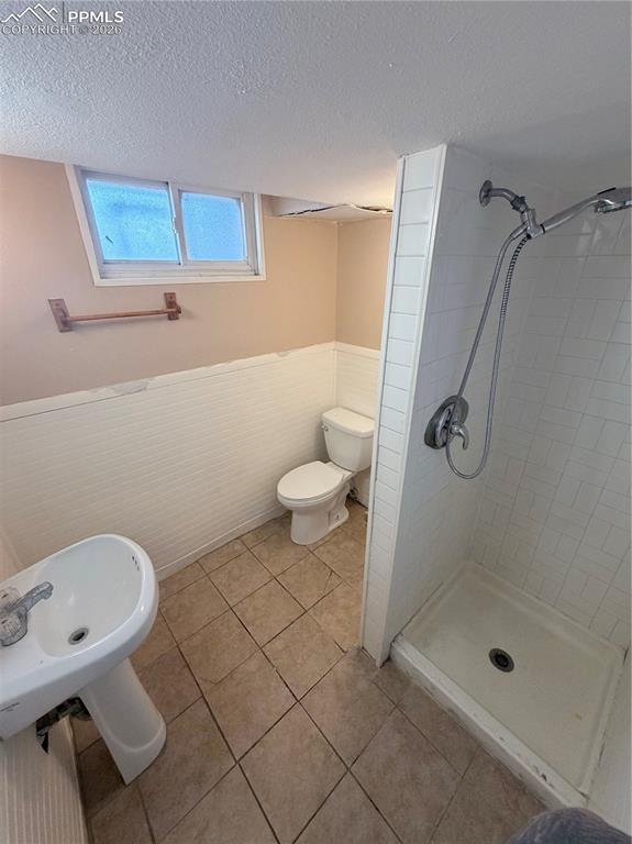 Full bathroom with wainscoting, a stall shower, a textured ceiling, and light tile patterned floors
