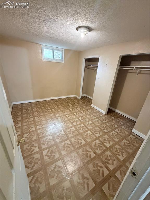 Unfurnished bedroom featuring two closets, a textured ceiling, and light floors