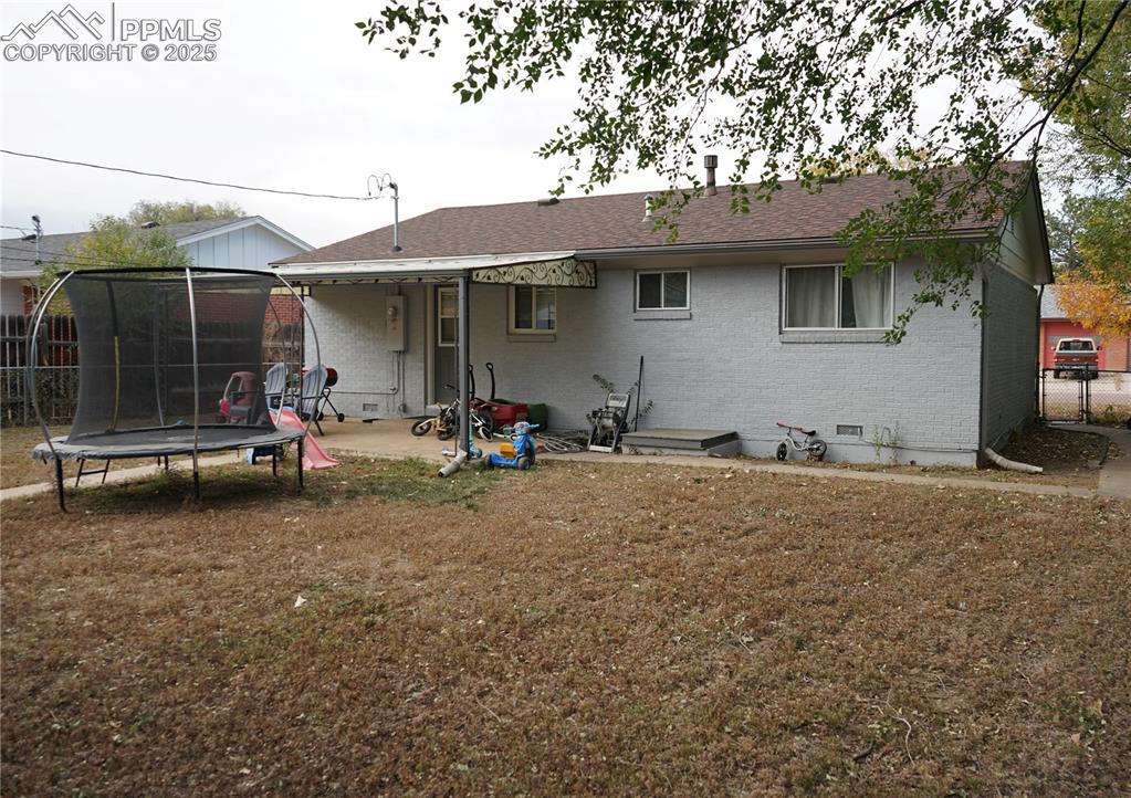 Rear view of house featuring a trampoline, brick siding, a patio, a shingled roof, and crawl space