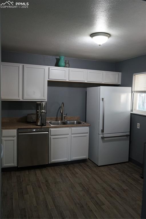 Kitchen featuring white cabinets, fridge, a textured ceiling, dark wood-type flooring, and white dishwasher