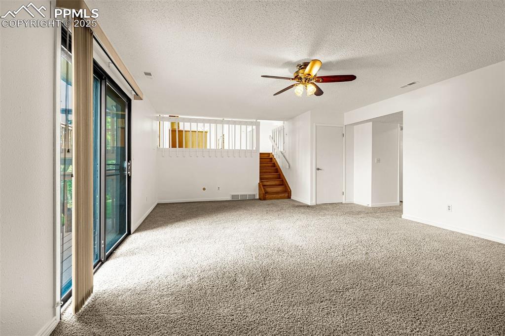 Empty room with light colored carpet, a textured ceiling, ceiling fan, and stairs