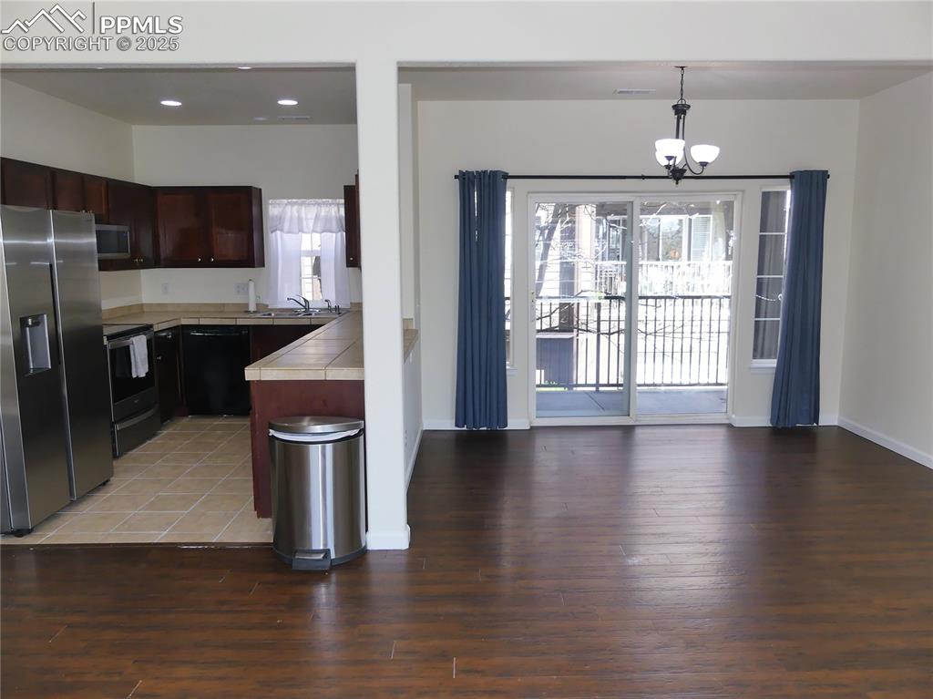 Kitchen featuring dark brown cabinetry, an inviting chandelier, light wood finished floors, tile countertops, and black appliances