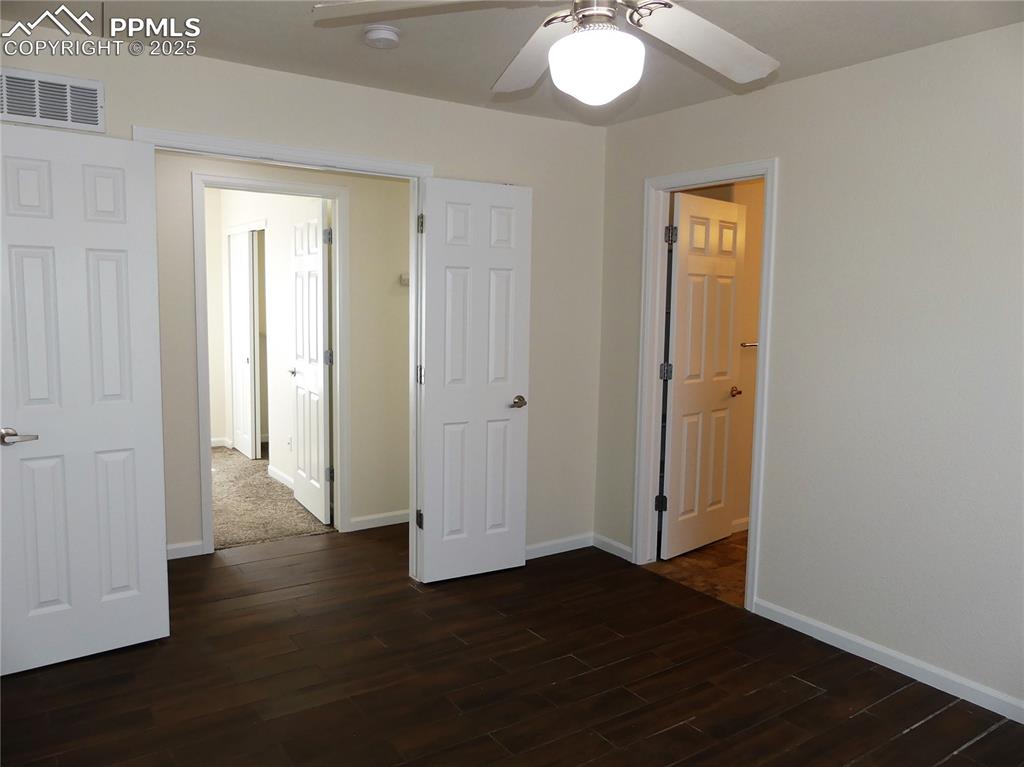 Primary bedroom with baseboards, a ceiling fan, dark wood finished floors, and visible vents