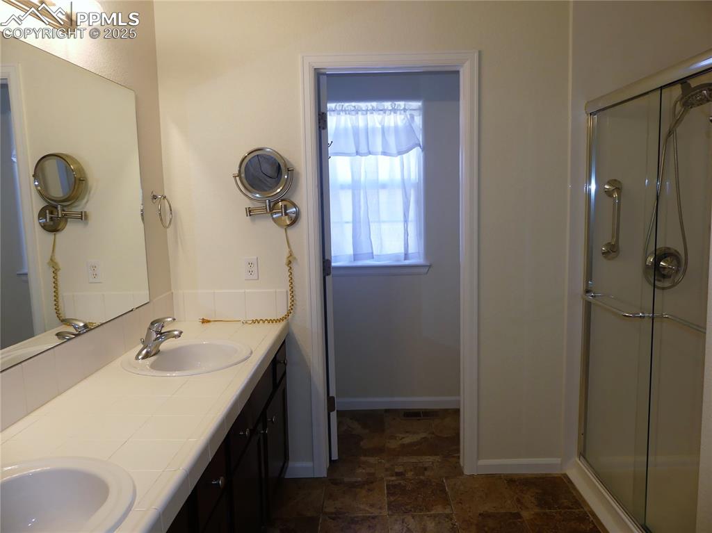 Bathroom featuring double vanity, stone finish flooring, a sink, and a stall shower