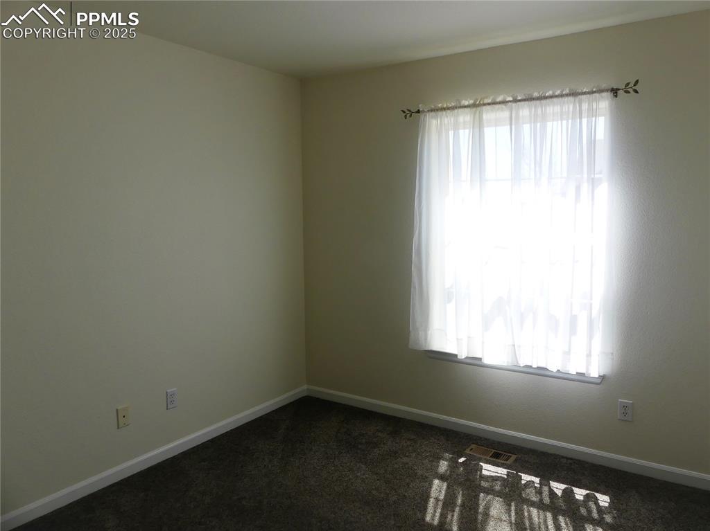 Unfurnished room with baseboards, visible vents, and dark carpet