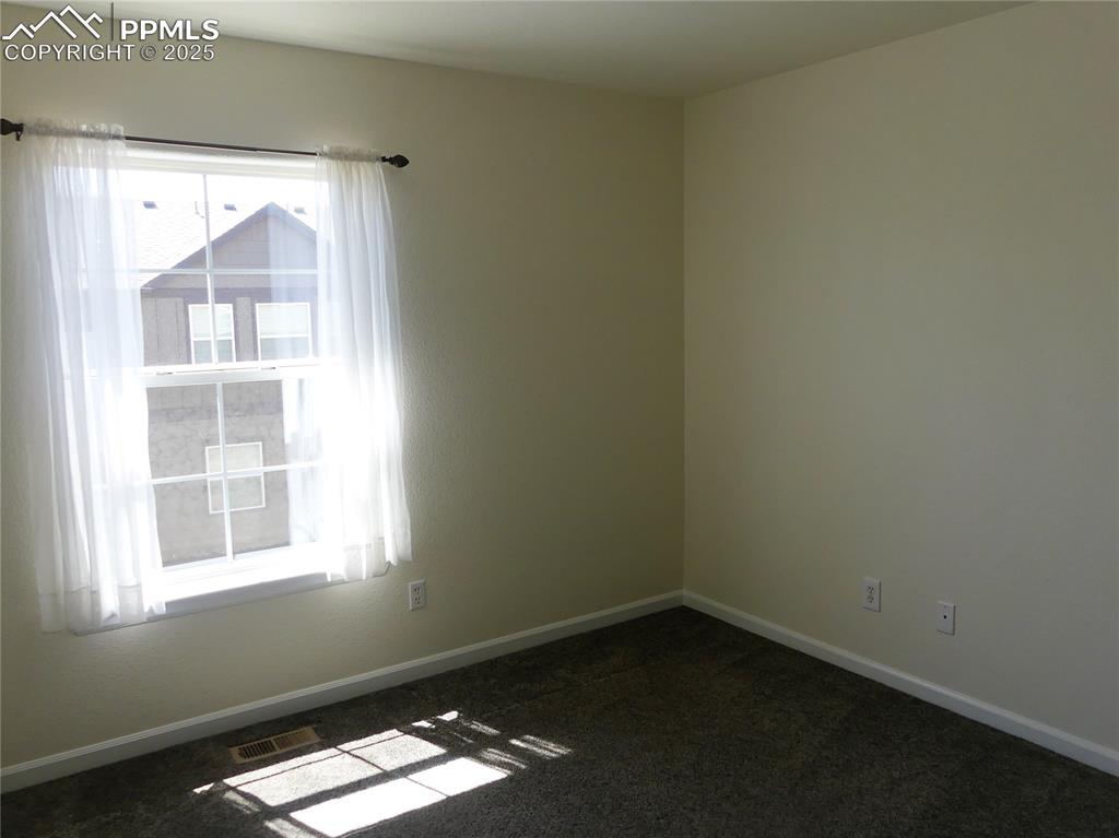 Empty room featuring visible vents, baseboards, and dark carpet