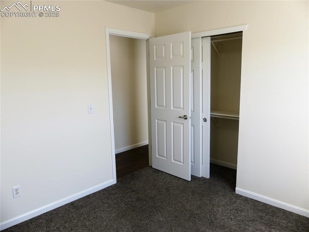 Unfurnished bedroom with baseboards, a closet, and dark carpet