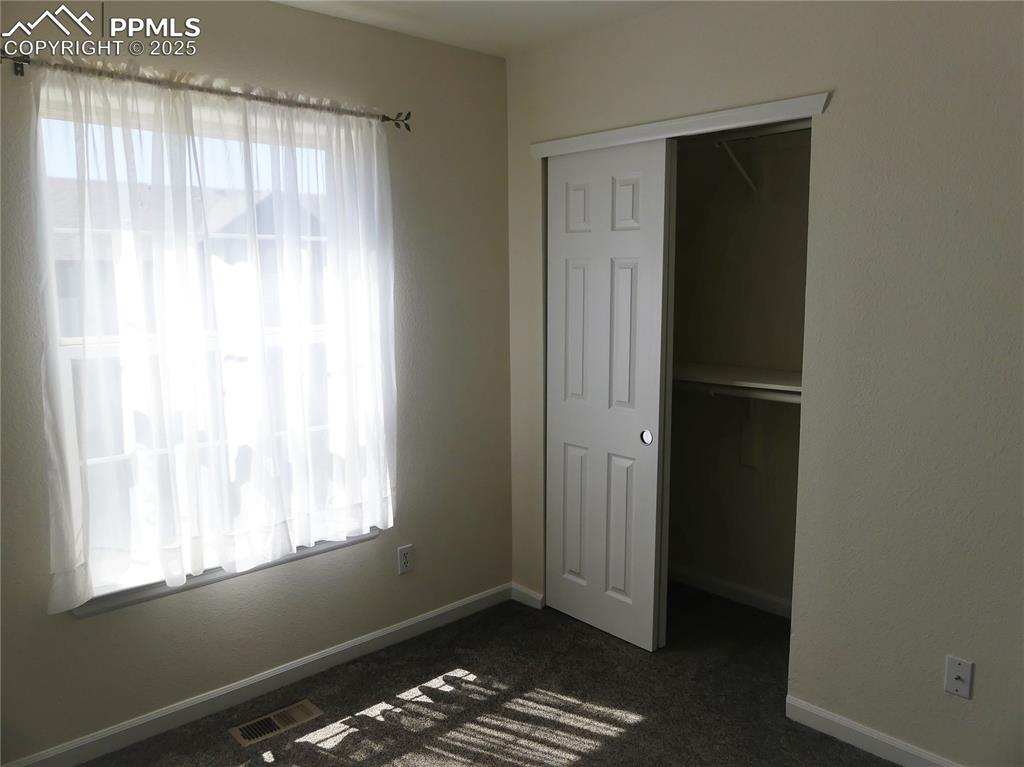 Unfurnished bedroom with baseboards, a closet, dark colored carpet, and visible vents