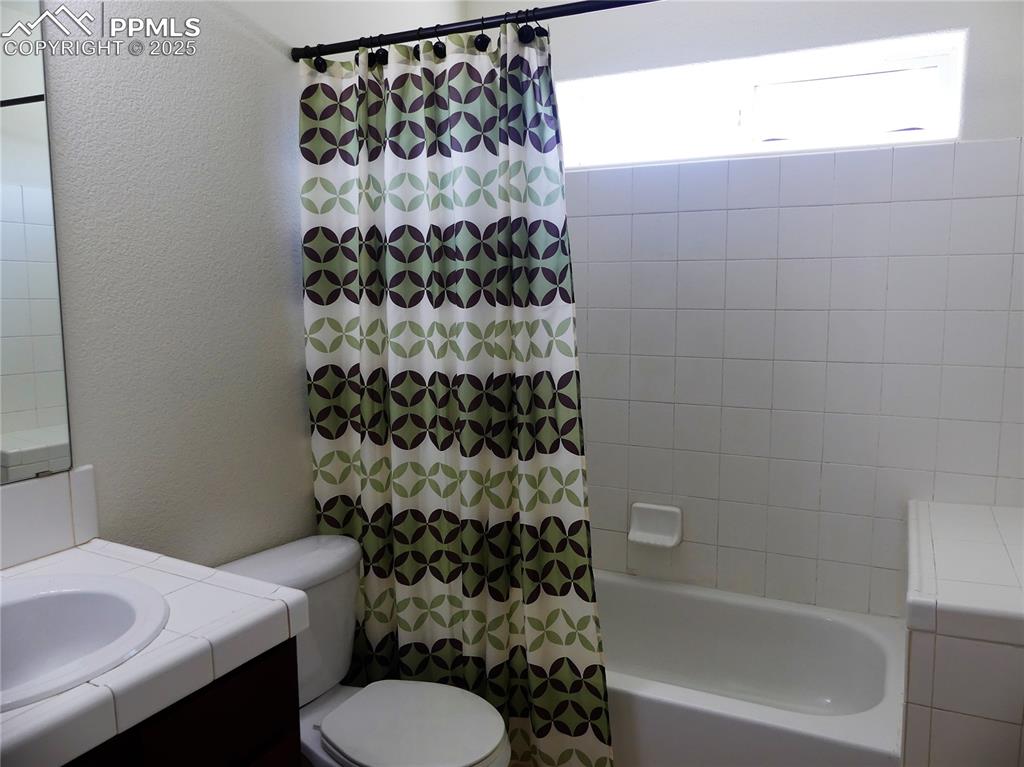 Bathroom with vanity, a textured wall, toilet, and shower / bath combination with curtain