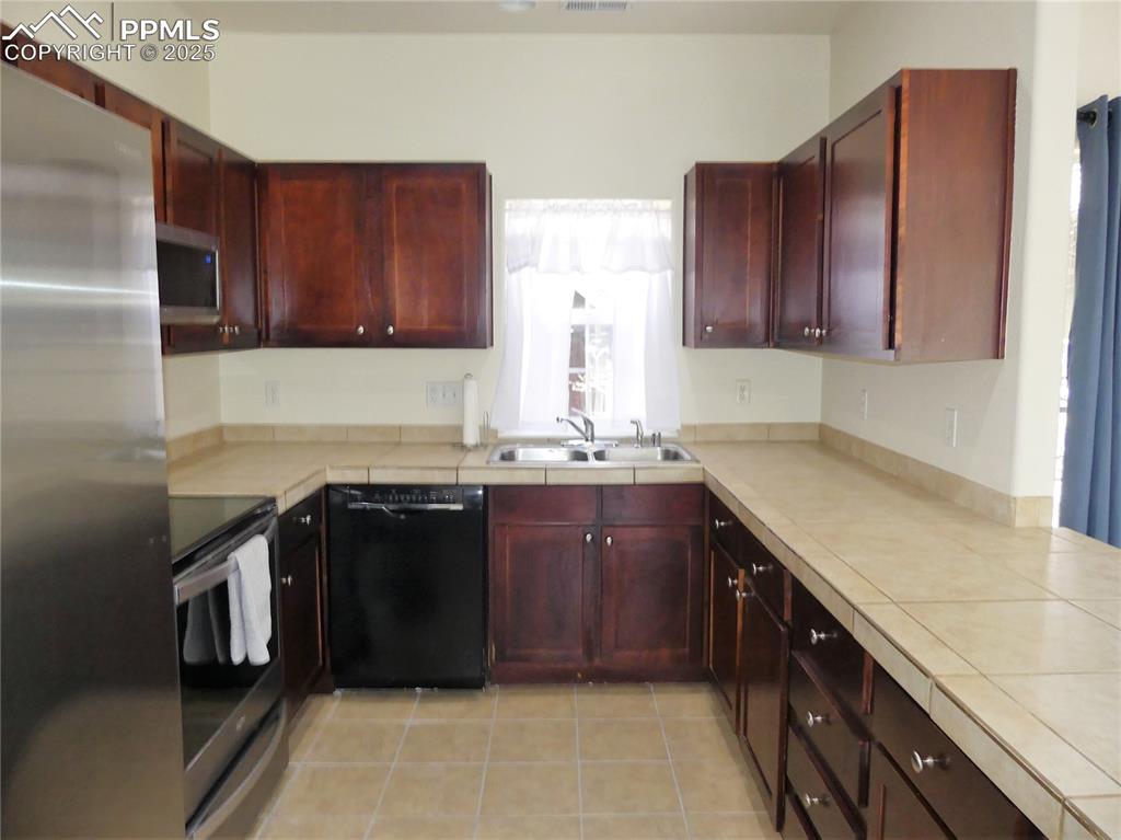 Kitchen with a sink, stainless steel appliances, tile countertops, light tile patterned floors, and reddish brown cabinets