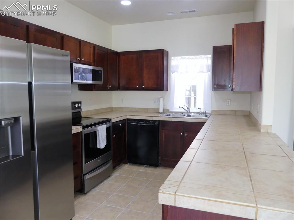 Kitchen with light tile patterned flooring, reddish brown cabinets, a sink, and stainless steel appliances