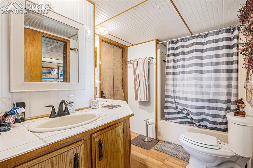 Full bath featuring vanity, shower / bath combo with shower curtain, toilet, and wood finished floors
