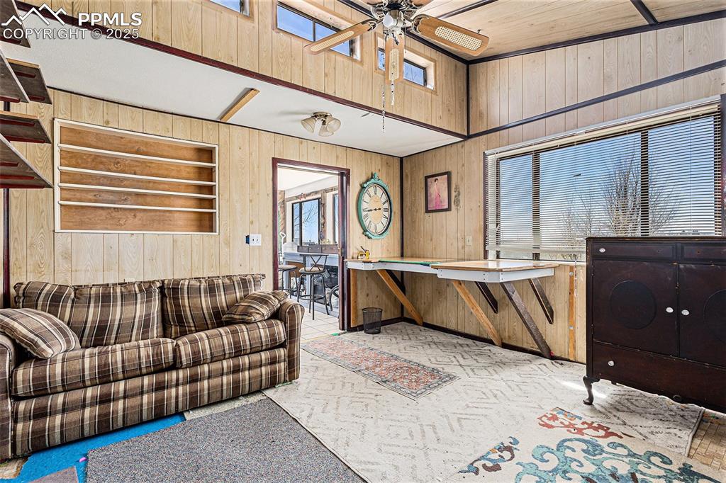 Carpeted living area with a ceiling fan, wood walls, and a healthy amount of sunlight