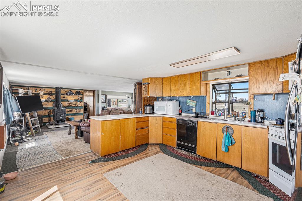 Kitchen featuring a wood stove, a peninsula, white appliances, light countertops, and light wood-style flooring