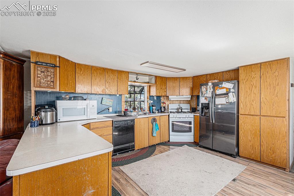 Kitchen featuring a peninsula, white appliances, light countertops, brown cabinets, and light wood-style flooring
