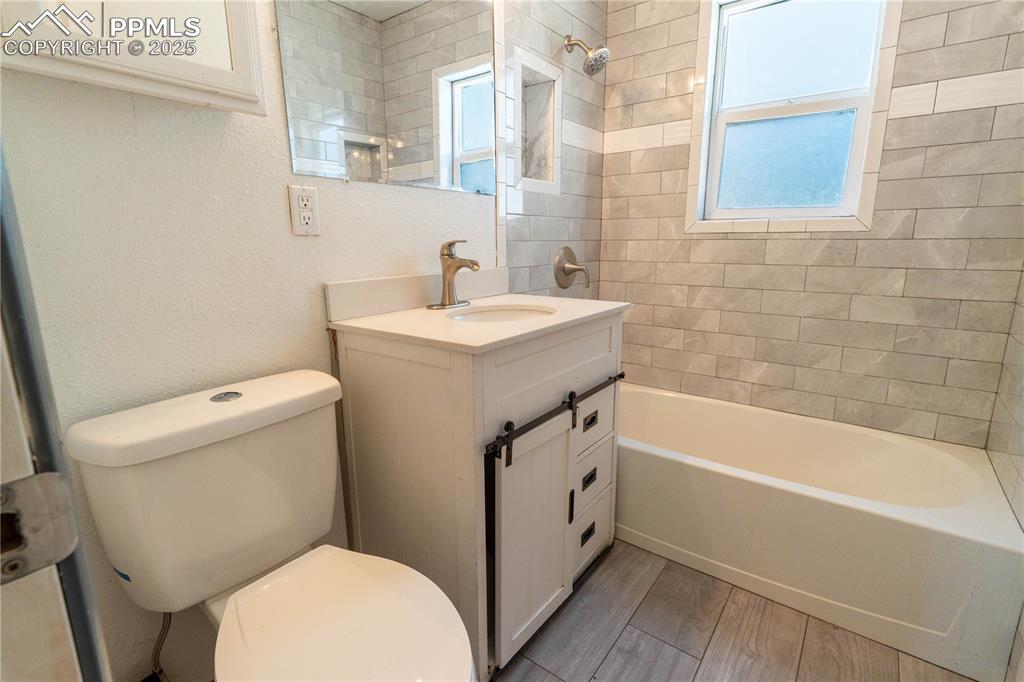 Bathroom featuring vanity, healthy amount of natural light, shower / washtub combination, a textured wall, and wood finish floors