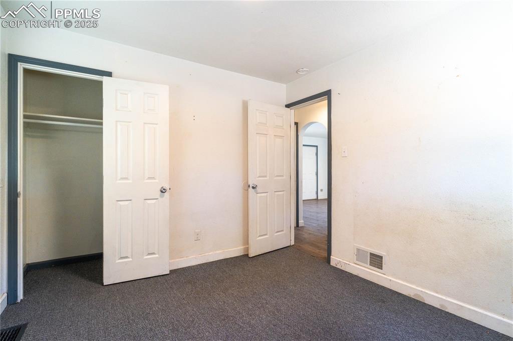 Unfurnished bedroom with arched walkways, dark colored carpet, and a closet