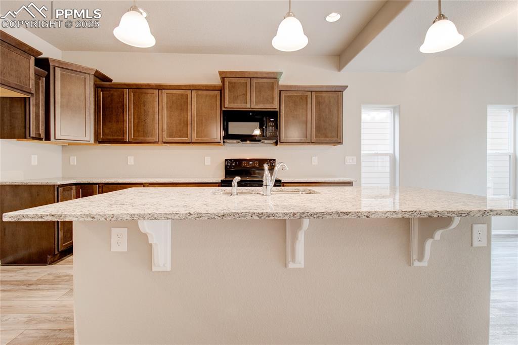 Kitchen with light wood-style flooring, decorative light fixtures, a center island with sink, a breakfast bar area, and recessed lighting