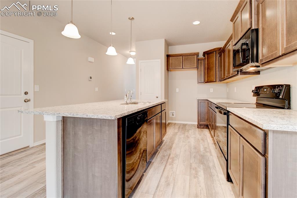 Kitchen featuring black appliances, recessed lighting, hanging light fixtures, light stone countertops, and a center island with sink