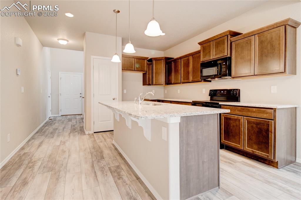 Kitchen featuring decorative light fixtures, black appliances, a kitchen breakfast bar, light wood finished floors, and brown cabinetry