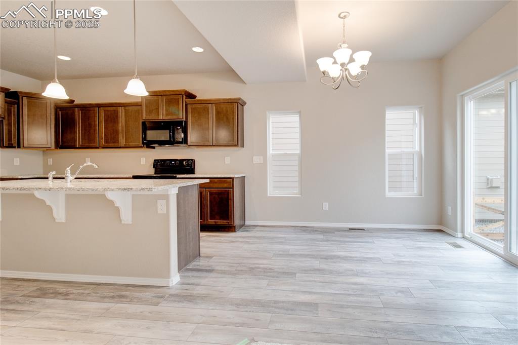Kitchen featuring a breakfast bar, brown cabinets, light wood finished floors, a chandelier, and hanging light fixtures