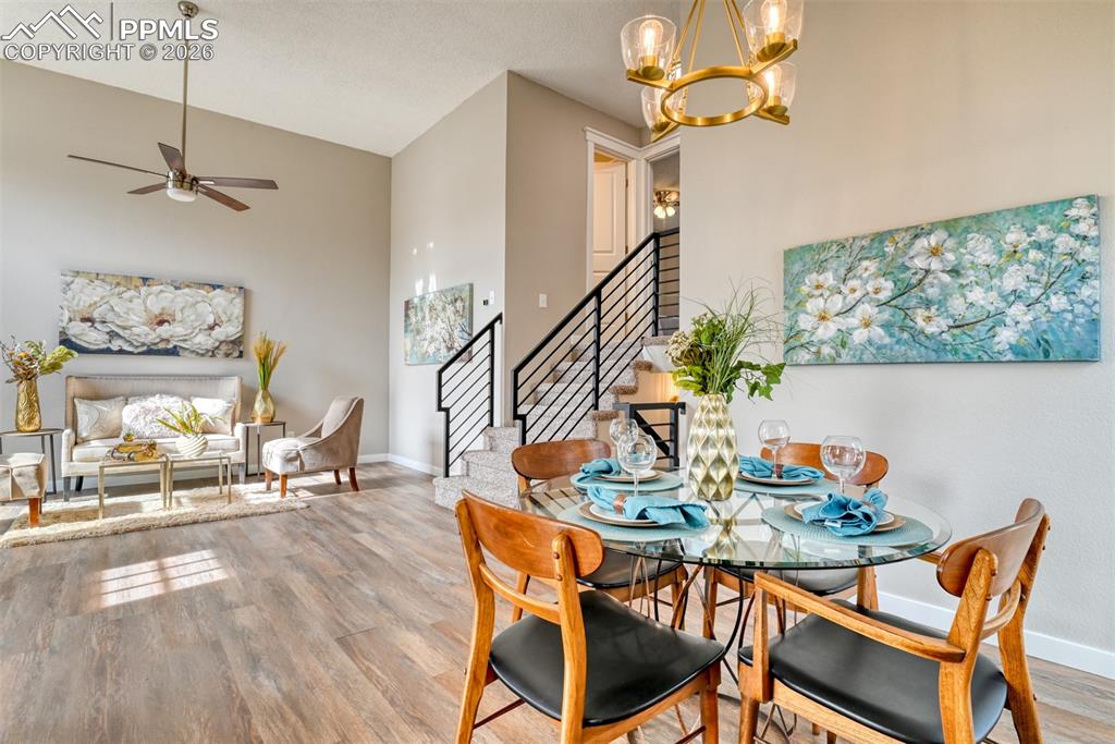 Dining space featuring wood finished floors, a chandelier, a fireplace, lofted ceiling, and a ceiling fan
