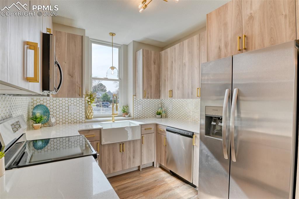Kitchen with stainless steel appliances, light stone counters, light wood finish cabinetry, pendant lighting, and light wood-type flooring