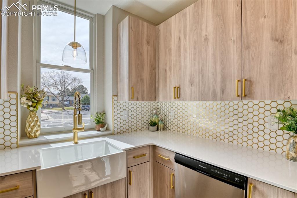 Kitchen with modern cabinets, dishwasher, light stone countertops, light wood finish cabinetry, and hanging light fixtures