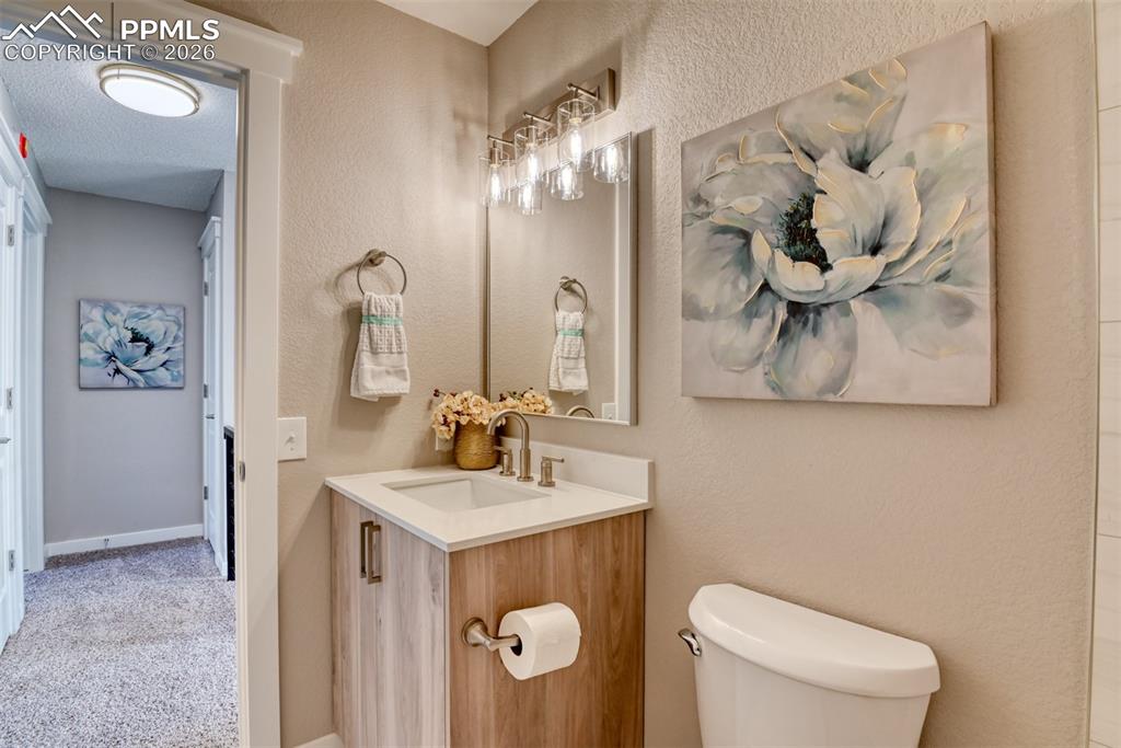 Half bath with vanity, light colored carpet, and a textured wall