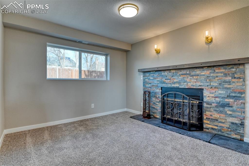 Unfurnished living room featuring carpet floors, a stone fireplace, and a textured ceiling
