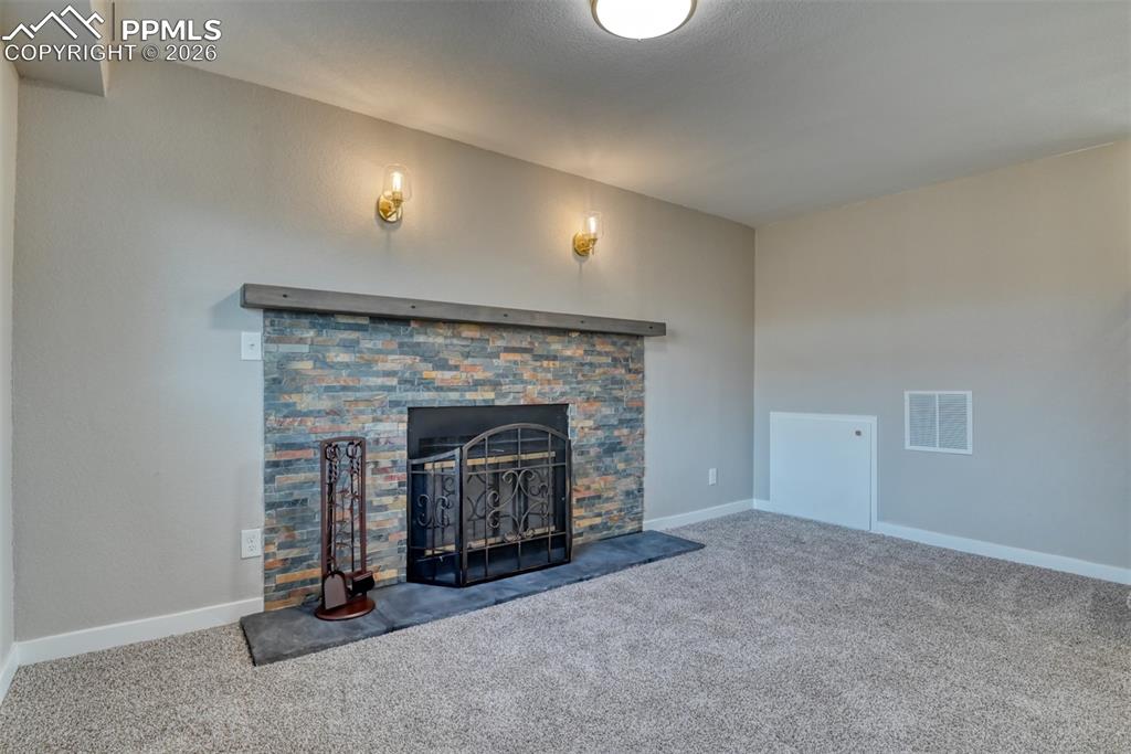 Unfurnished living room with carpet and a stone fireplace